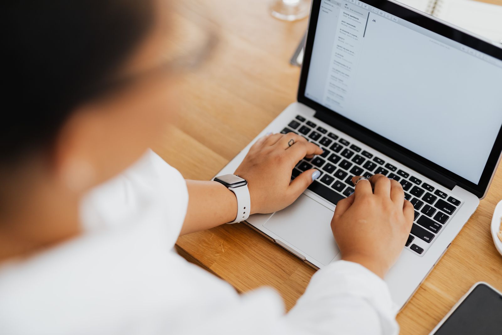 A woman typing an email on a laptop at a wooden desk