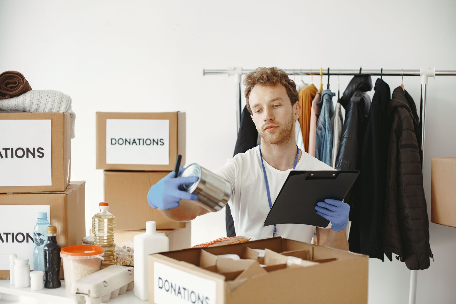 A volunteer with a clipboard logging canned food and clothing in donation boxes