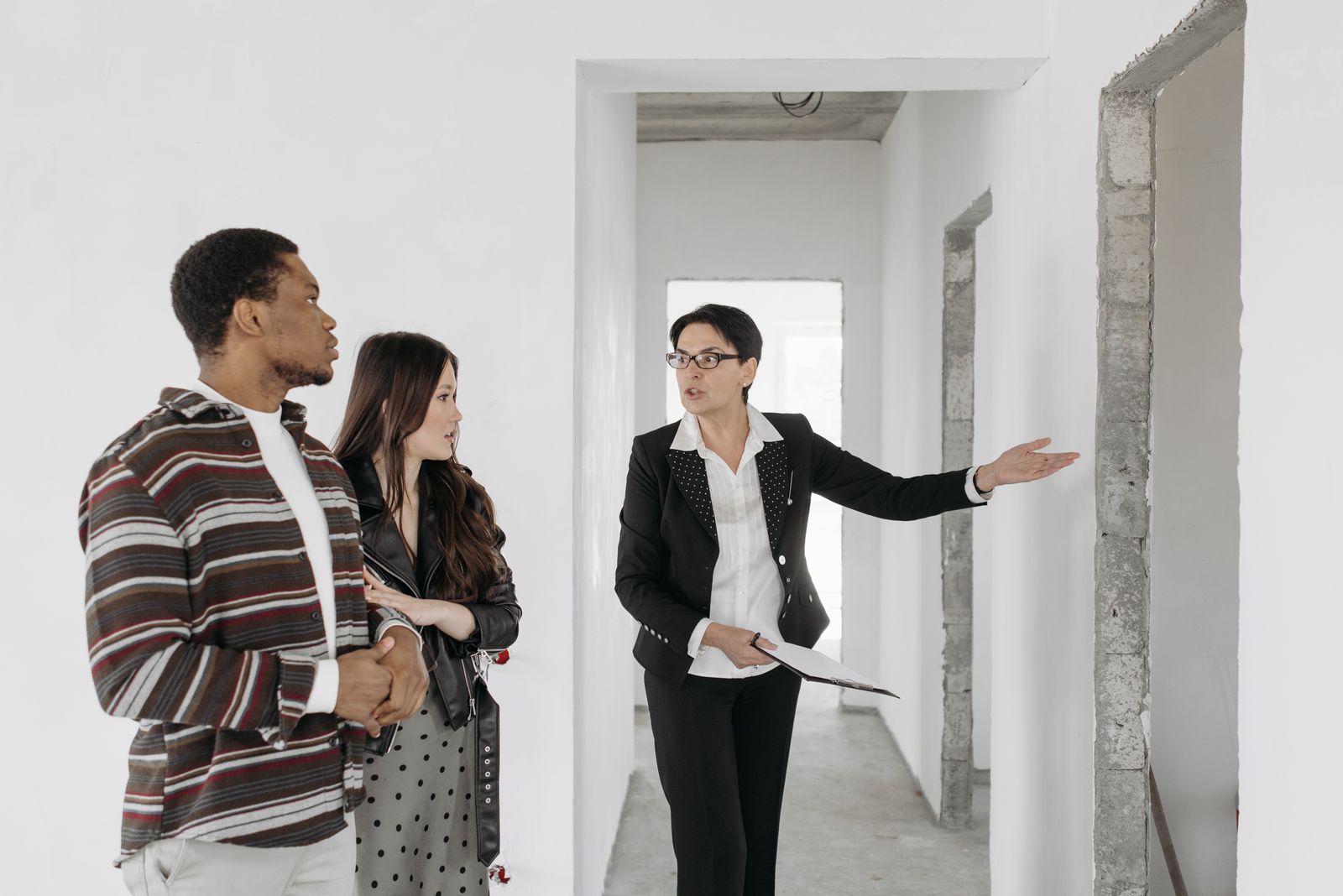 A real estate agent with a clipboard showing a couple around an unfinished home