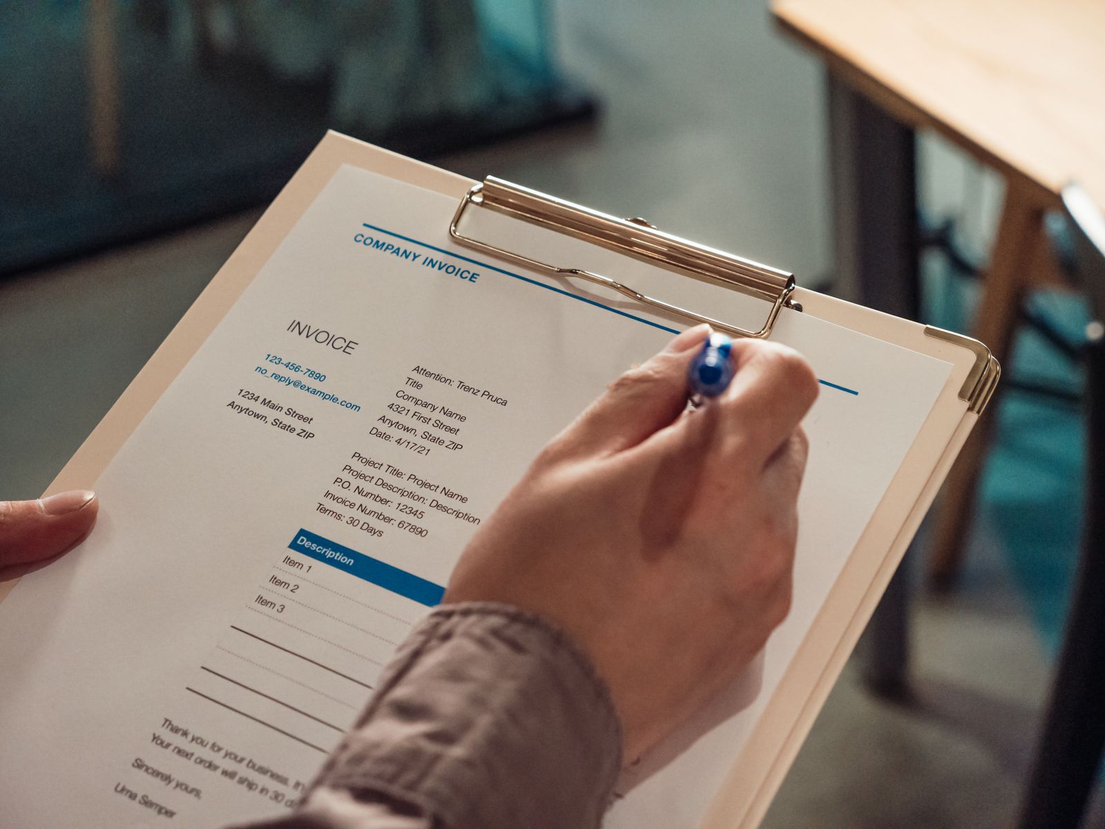 A hand with a blue pen filling in a printed company invoice on a clipboard