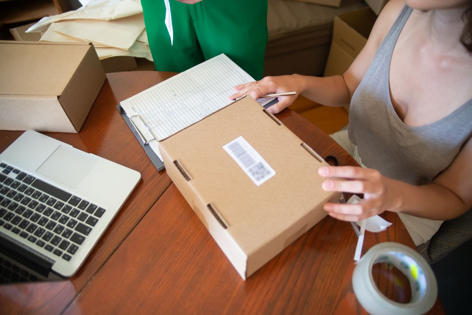 A woman labeling a shipping box for an online order next to a laptop and an order sheet