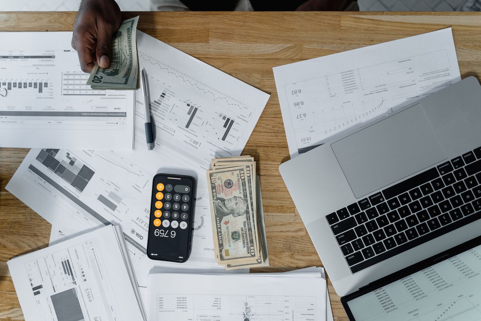 Overhead view of a desk with financial documents, cash and a laptop