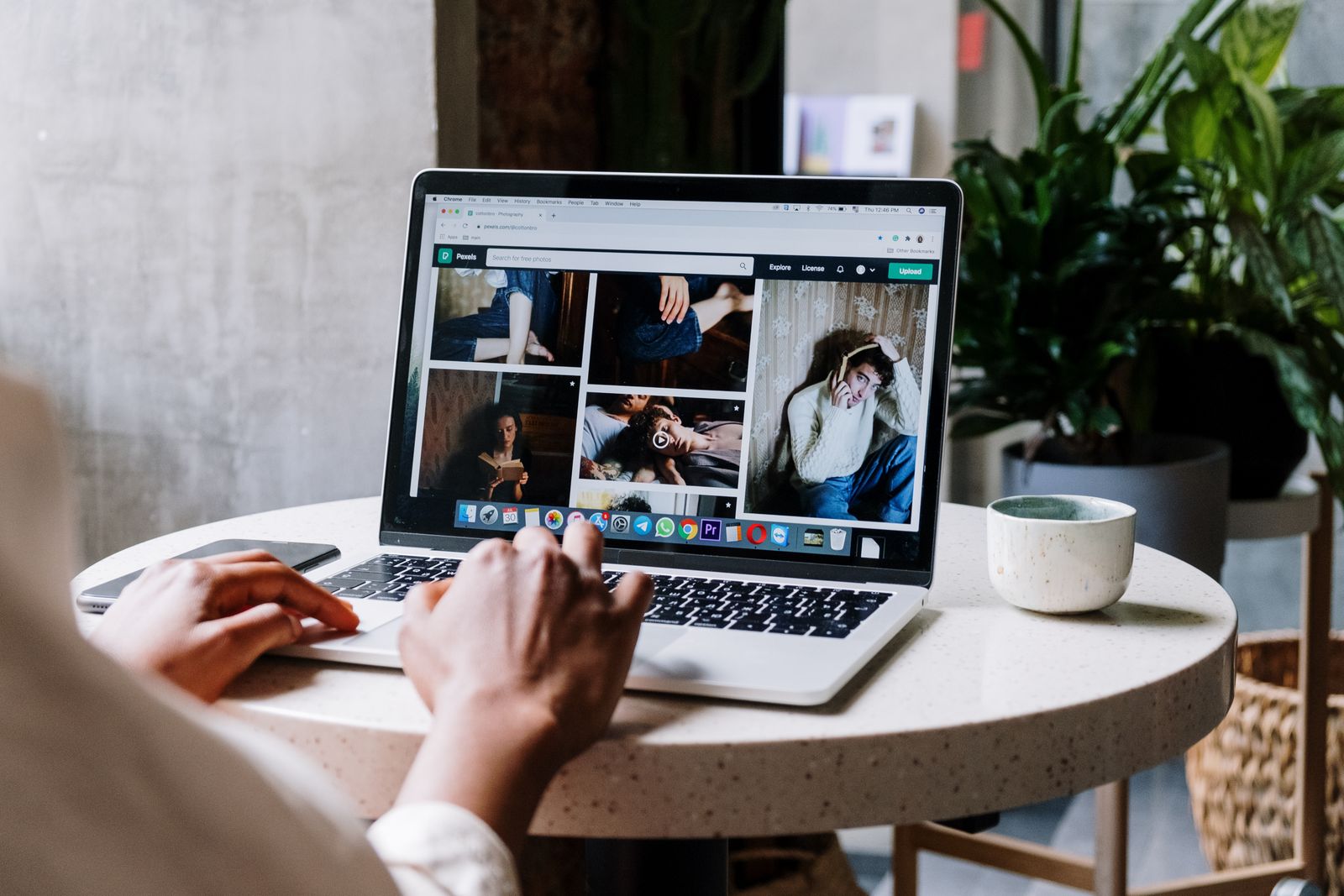 A person at a round café table browsing a photo gallery website on a laptop