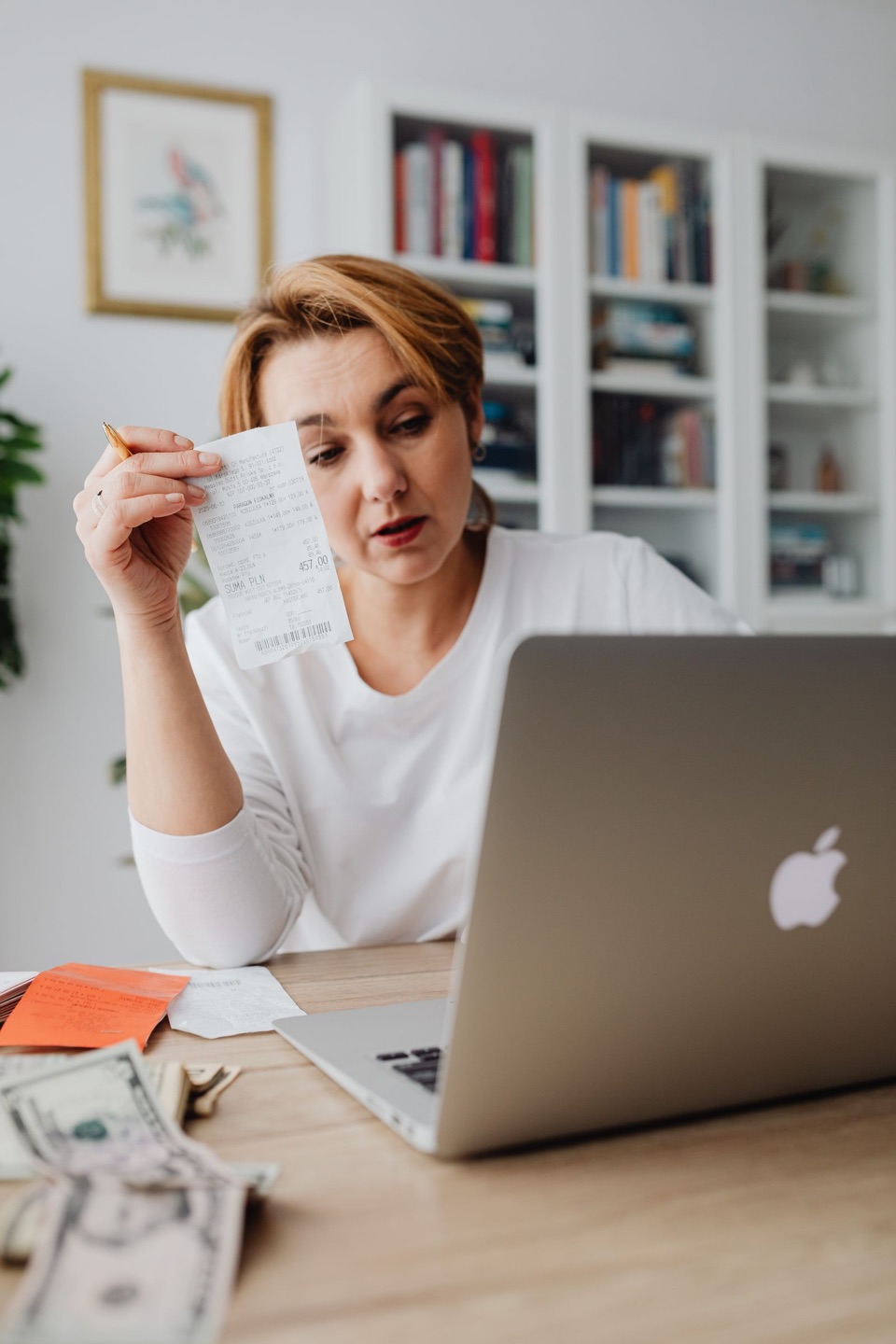 A business owner at her laptop holding up a receipt, with cash on the desk